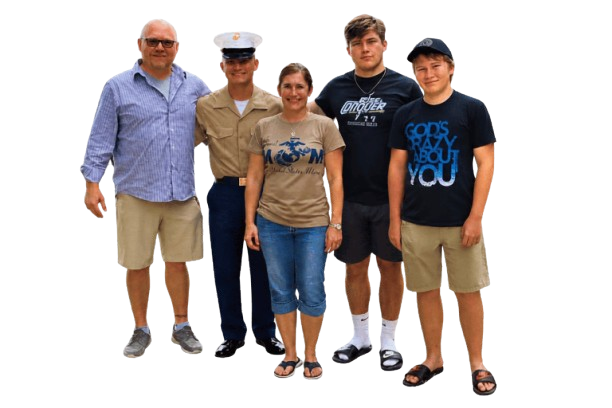 The Boval Family Five people stand in a row, smiling. One wears a military uniform, while the others are dressed casually in shorts and t-shirts. Behind them, the plain white background suggests they could be standing under retractable awnings on a sunny day.